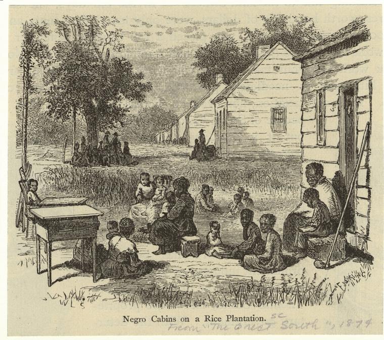 Black adults and children sit together outside in the grass. To the right is a row of small cabins and in the background is another grouping of people.