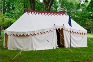 Large white tent with red trim, set up on a grassy lawn in front of trees. 