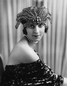 A portrait of a woman with an off the shoulder dress on and wearing a beaded decorative piece on top of head