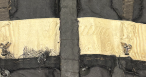 Shows a cream colored label for Paquin surrounding by the boning structure of the bodice. The structure is black in color.