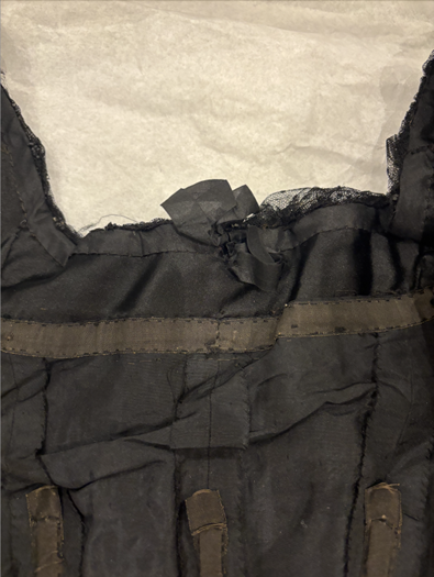 Shows the original neckline and added neckline. See the boning structure of the dress and how it changed. There is tulle along the top. Can see where the material was grabbed to change neckline.