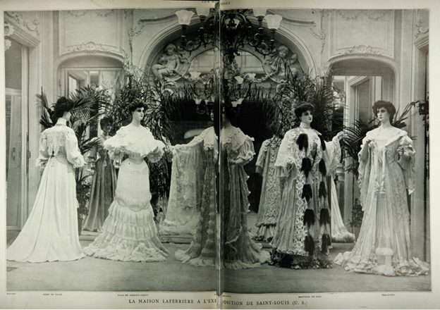 Shows a group of women wearing ruffled lace floor length dresses. Standing in front of an arched hallway
