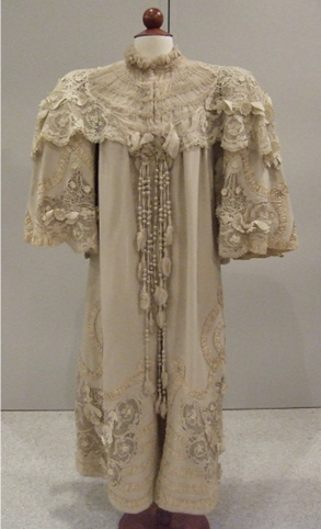 A off white cloak with a ruffled lace collar, lace going down the center, and along the sides