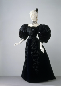 A black evening dress with massive puffy sleeves and detailing cording. The dress appears to have lace design with a slight ruff at the bust.